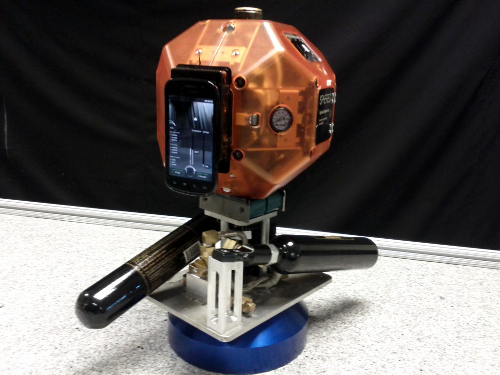 Satélite SPHERES equipado con un teléfono inteligente, imagen ilustrativa de la conexión entre móviles y satélites.
